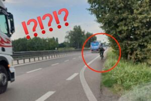 Ciclista in contromano sulla corsia di emergenza tra bici e autobus sulla strada statale in campagna.
