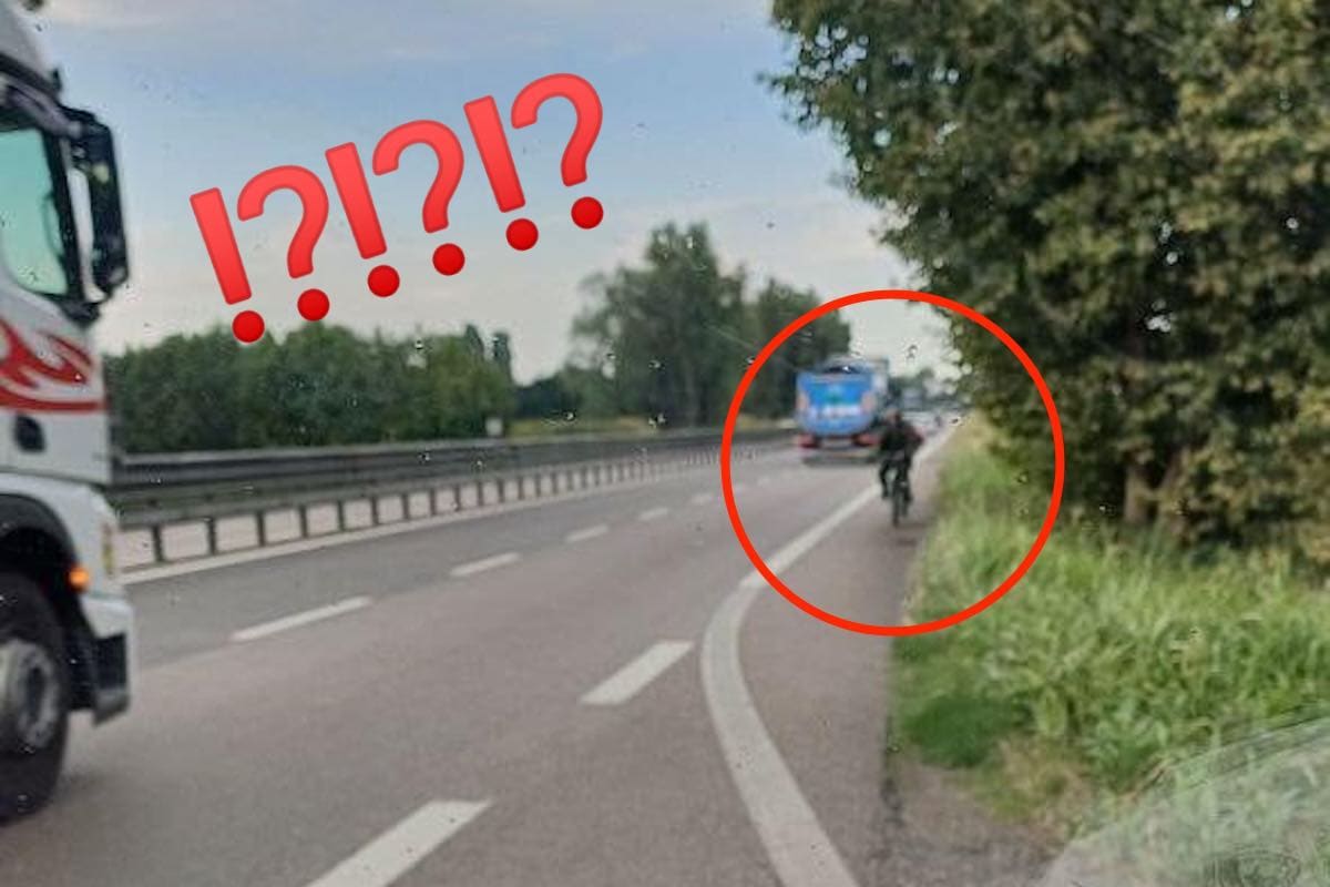 Ciclista in contromano sulla corsia di emergenza tra bici e autobus sulla strada statale in campagna.