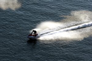 Persona in moto d’acqua rossa e bianca sfreccia sull’acqua lasciando una lunga scia di spruzzi.