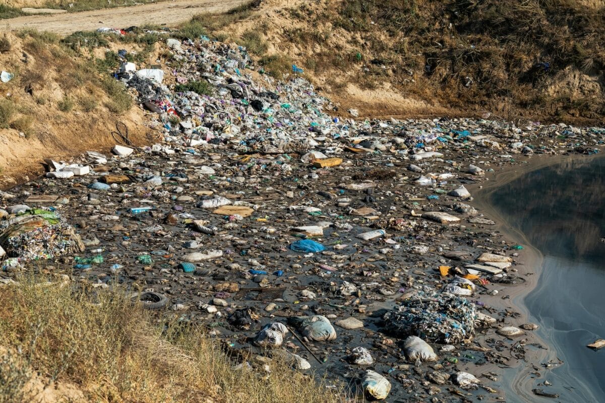 Rifiuti abbandonati e plastica ammassati sulle sponde di un corso d’acqua inquinato.