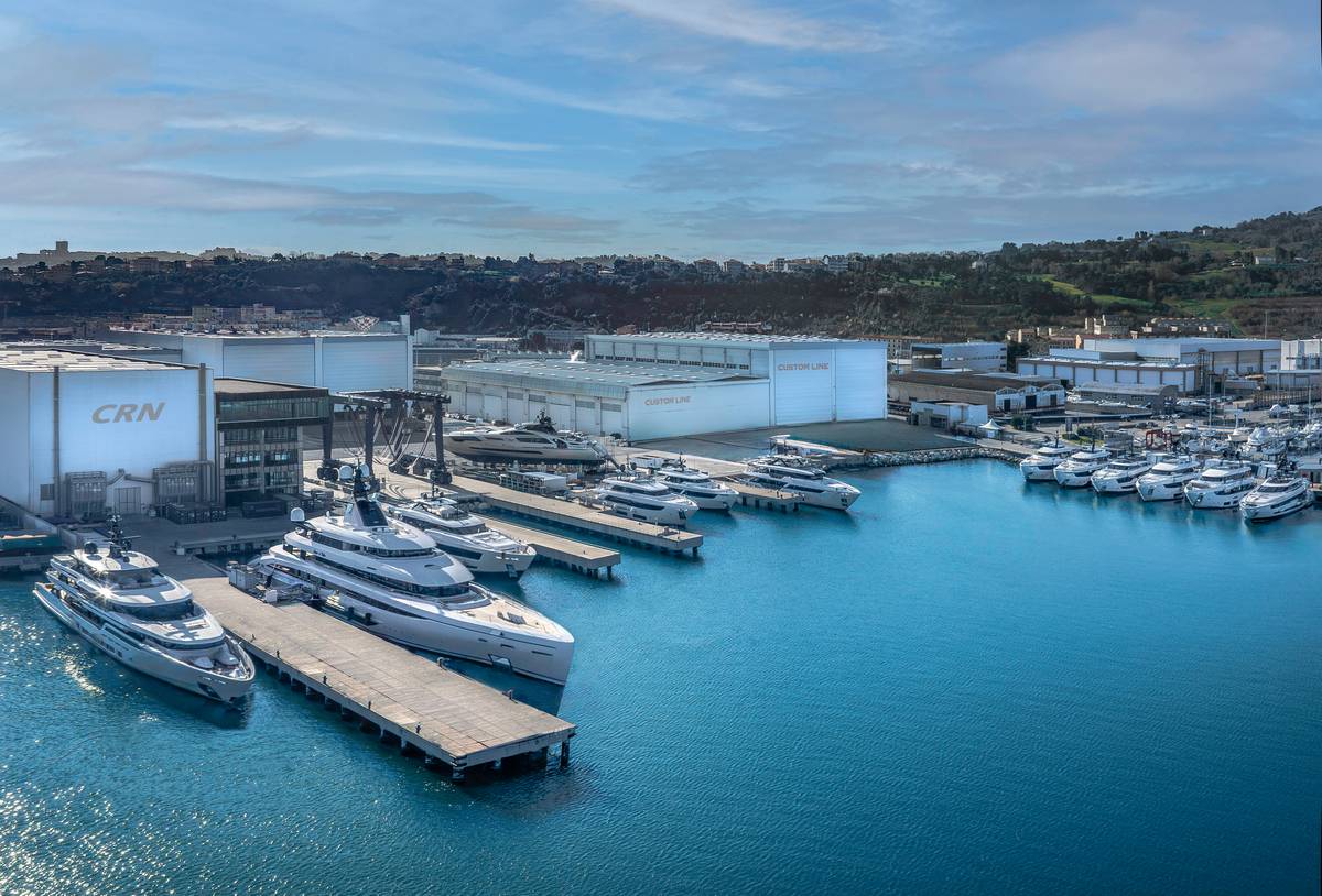 Porto turistico con yacht di lusso e strutture industriali, vista panoramica sul mare e le colline circostanti, focus su imbarcazioni di alta gamma e settore nautico di lusso.