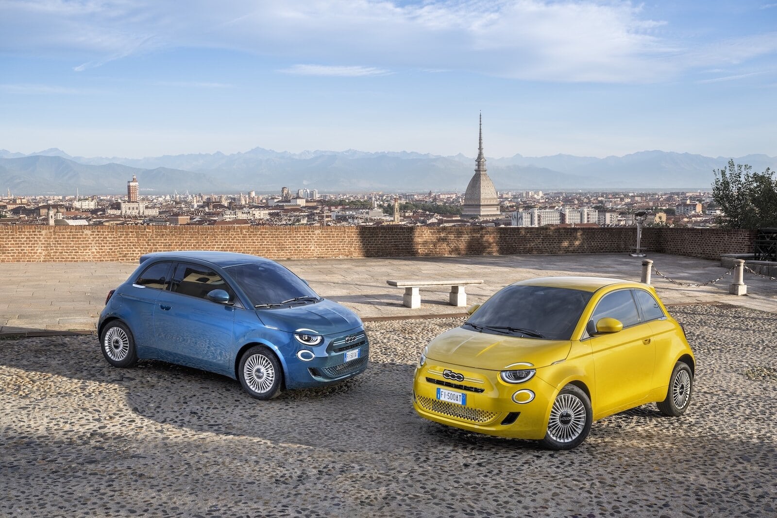 Due Fiat 500 Hybrid, una gialla e una blu, parcheggiate con vista panoramica su Torino, con la Mole Antonelliana e le Alpi sullo sfondo.