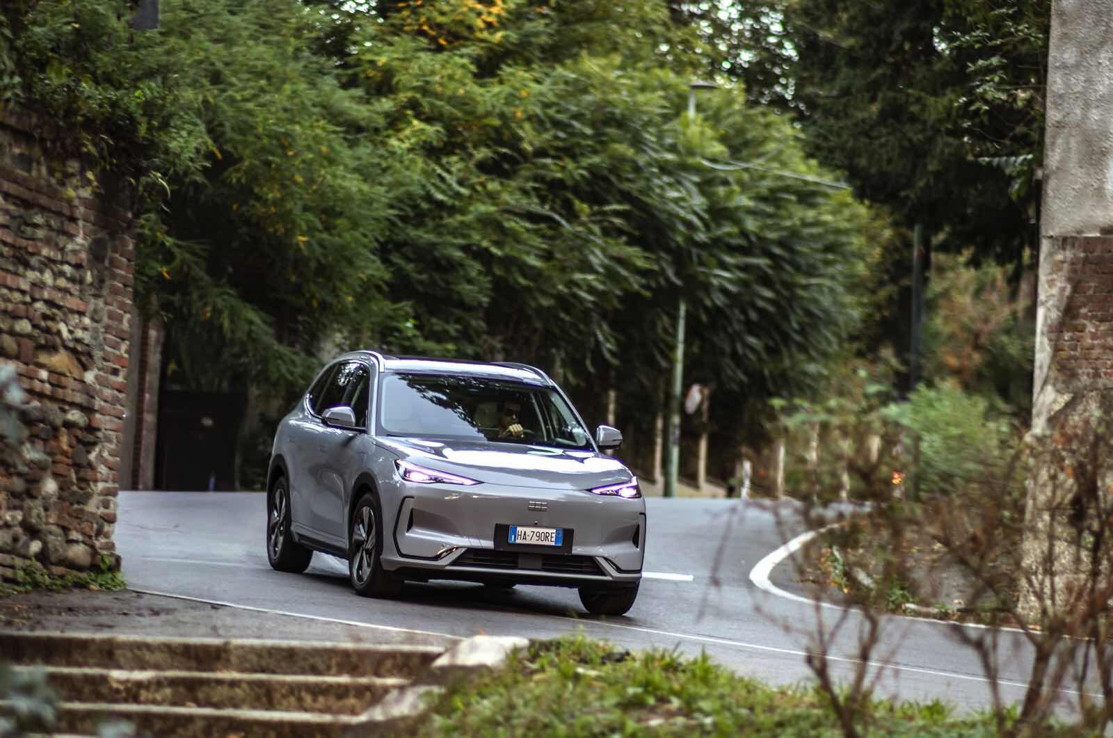 Auto elettrica Geely EX5 in movimento su strada di montagna immersa nel verde, veicolo sostenibile e innovativo.
