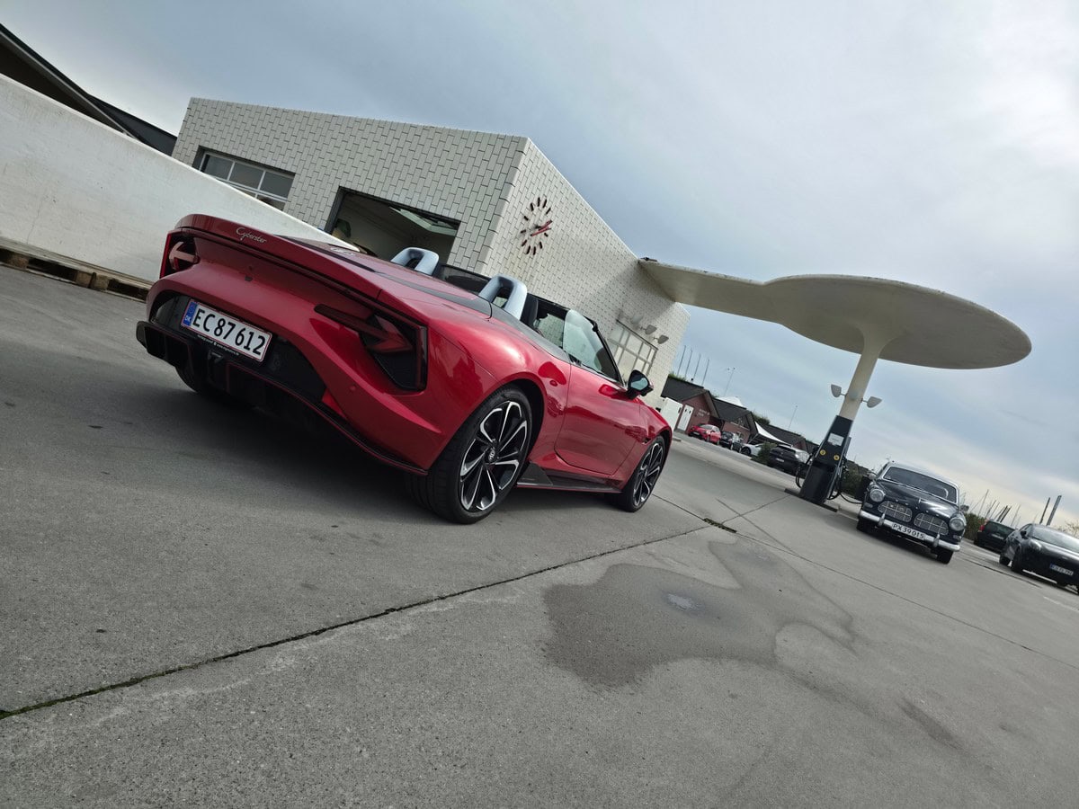 SUV della Lamborghini in stile convertibile con carrozzeria rossa, auto sportiva di lusso, parcheggiata davanti a una stazione di rifornimento con architettura moderna.