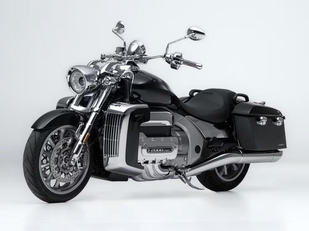 Moto cruiser Souo S2000 R nera e cromata su sfondo bianco, con borse laterali rigide, doppio scarico cromato e massiccio motore 2000 cc a sei cilindri.