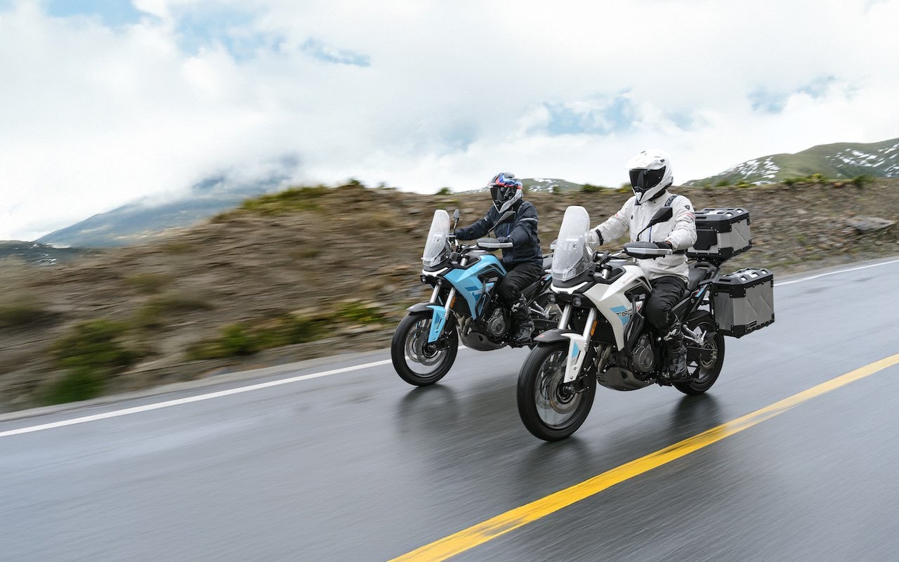 Due motociclisti percorrono una strada di montagna con le loro Morbidelli T502X, una azzurra e una bianca, sotto un cielo coperto da nuvole.