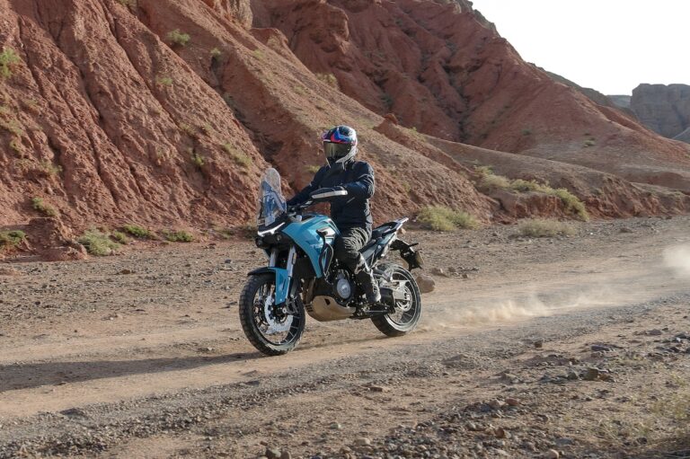 Un motociclista guida una Morbidelli T502X azzurra su una pista sterrata tra le rocce rosse, sollevando polvere mentre affronta il terreno arido.