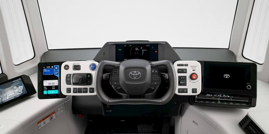 Vista frontale della plancia comandi del Toyota e-Palette, con volante, schermi digitali e comandi touch, progettati per la guida autonoma e il monitoraggio del veicolo.