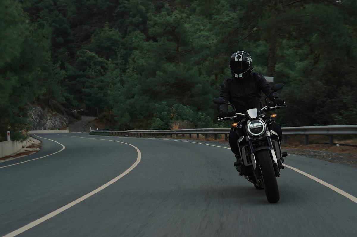 Moto naked moderna in viaggio su strada panoramica tra gli alberi, guida di un motociclista con casco integrale, stile dinamico e avventuroso, perfetta per appassionati di motori e road trip.