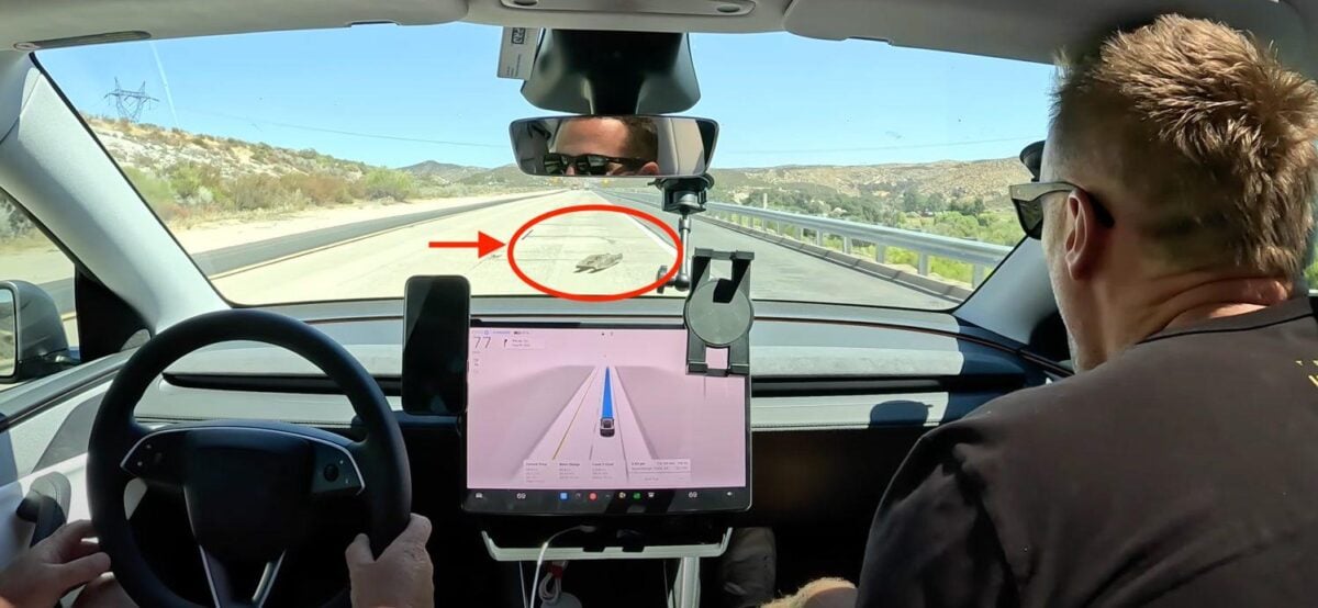 Autista in auto con sistema di assistenza alla guida su strada desertica, display touchscreen e fotocamera di sicurezza frontale.