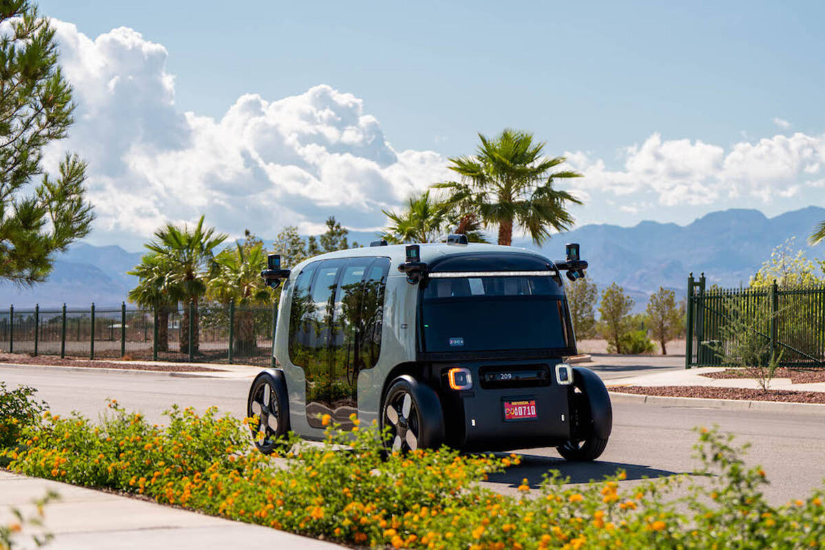 Robotaxi Zoox circola in una zona tranquilla con palme, fiori e cielo limpido, evidenziando il suo design futuristico.