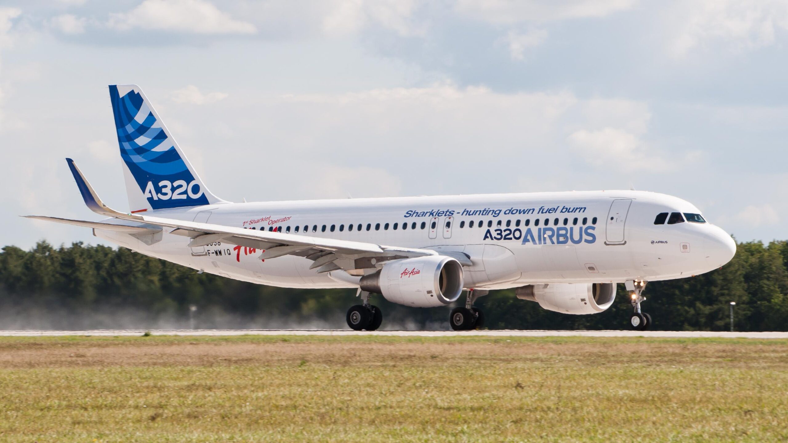 A320 Airbus in fase di atterraggio su pista con nuvole e cielo sereno sullo sfondo.