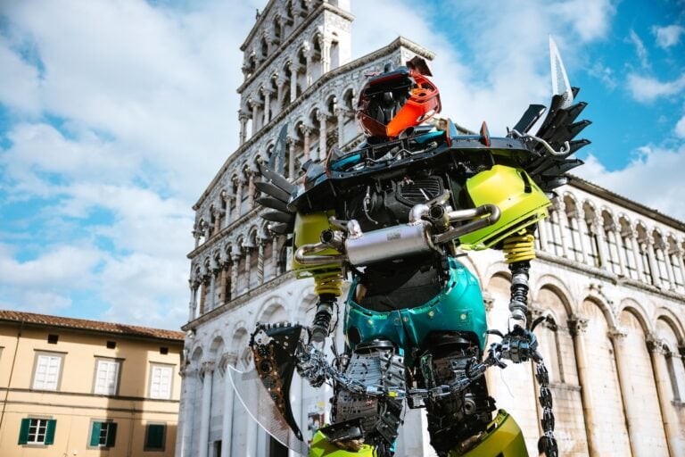 Motore robotico in stile fantascienza davanti al duomo di pisa, scultura tecnologica futuristica, installazione artistica innovativa, rappresentazione di intelligenza artificiale e robotica, scultura moderna e avveniristica.