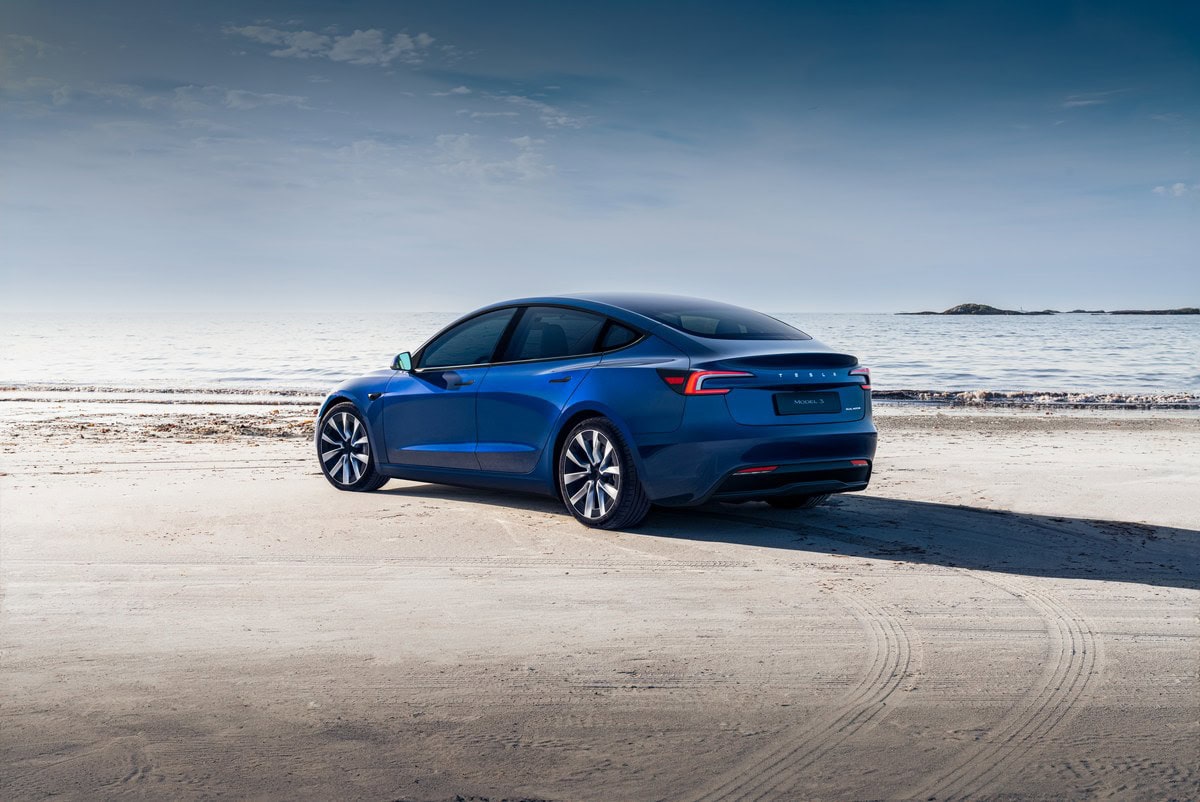 Auto elettrica Tesla Model 3 blu in spiaggia con vista sul mare al tramonto, veicolo innovativo e sostenibile, design moderno e tecnologia avanzata.
