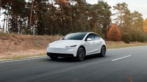 Auto elettrica moderna in movimento lungo strada di campagna con alberi autunnali.