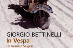 Scooter Vespa Piaggio con decalcomanie vintage sulla spiaggia sabbiosa, ombra proiettata sulla sabbia, destinazione in Vietnam, viaggio da Roma a Saigon.