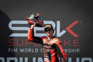 Casco da corsa Monster Energy e pilota di motociclismo in abbigliamento racing, in posa vittoriosa sul podio del Superbike FIM World Championship.