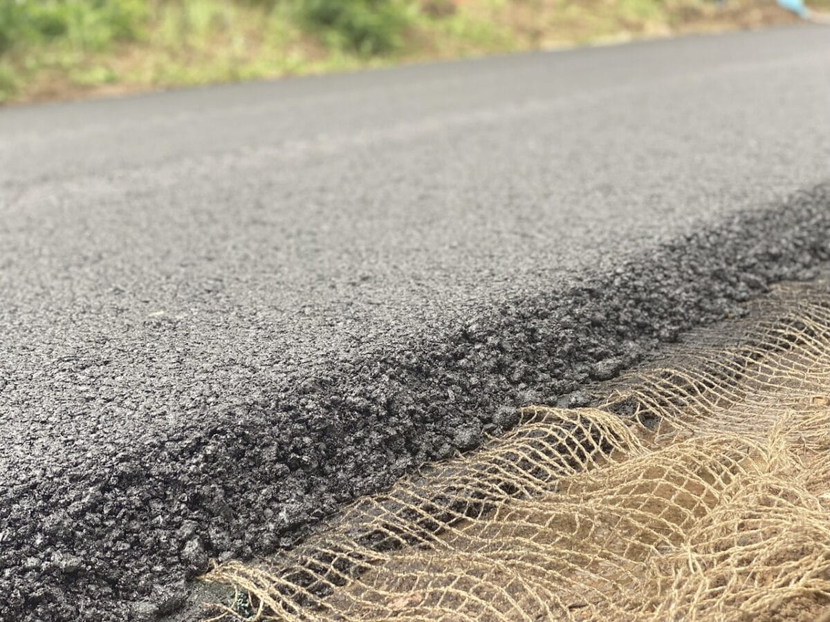 Asfalto strada fessurata durante la ristrutturazione di una carreggiata asfaltata, lavori di mantenimento stradale, superficie stradale curata e in fase di rinnovo, dettaglio tessuto non tessuto sotto l'asfalto, materiali da costruzione stradale.