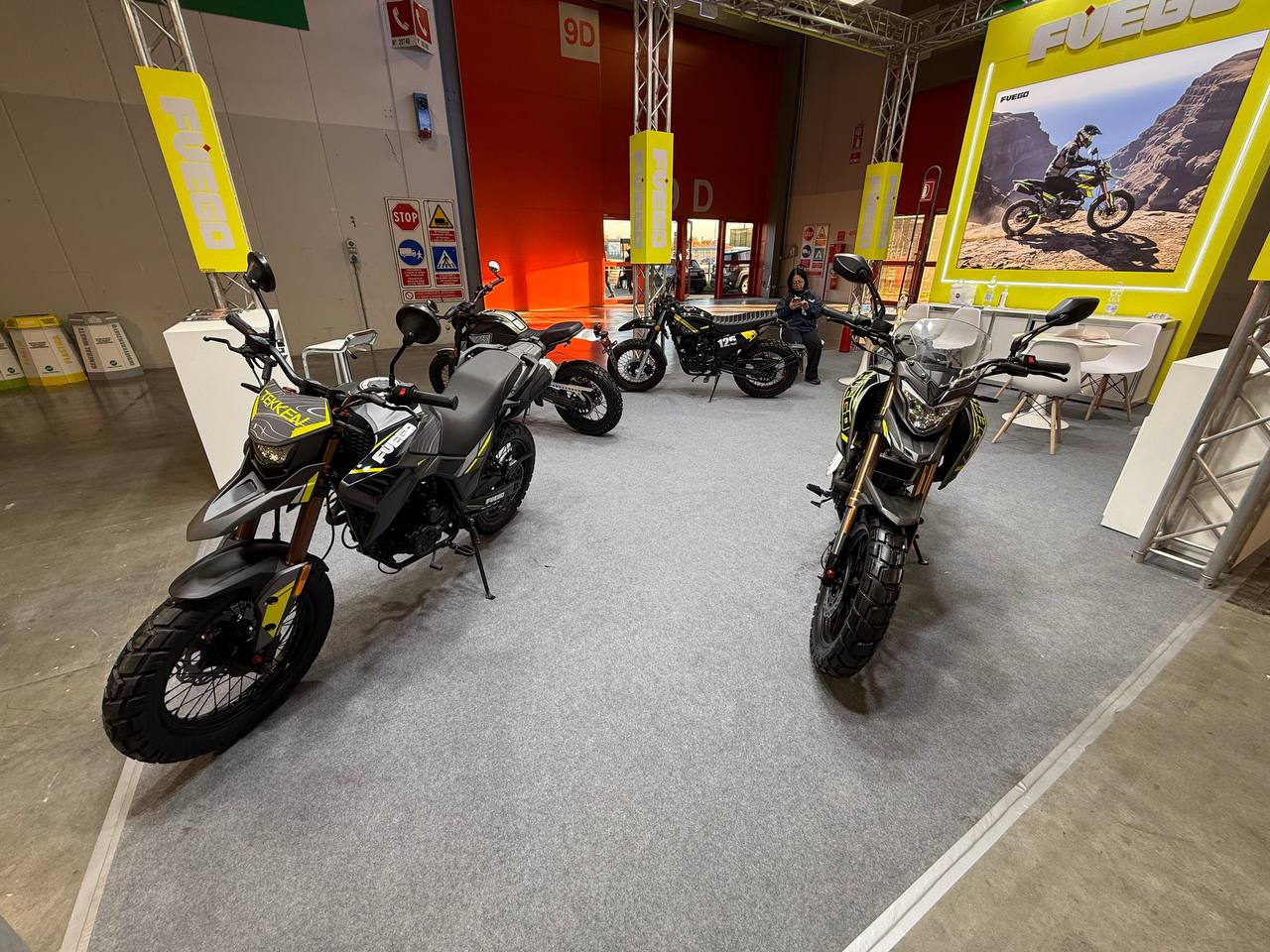 Moto Fuego e motociclette fuoristrada presso stand fieristico FUEGO, esposizione veicoli elettrici per appassionati di motori ecologici.