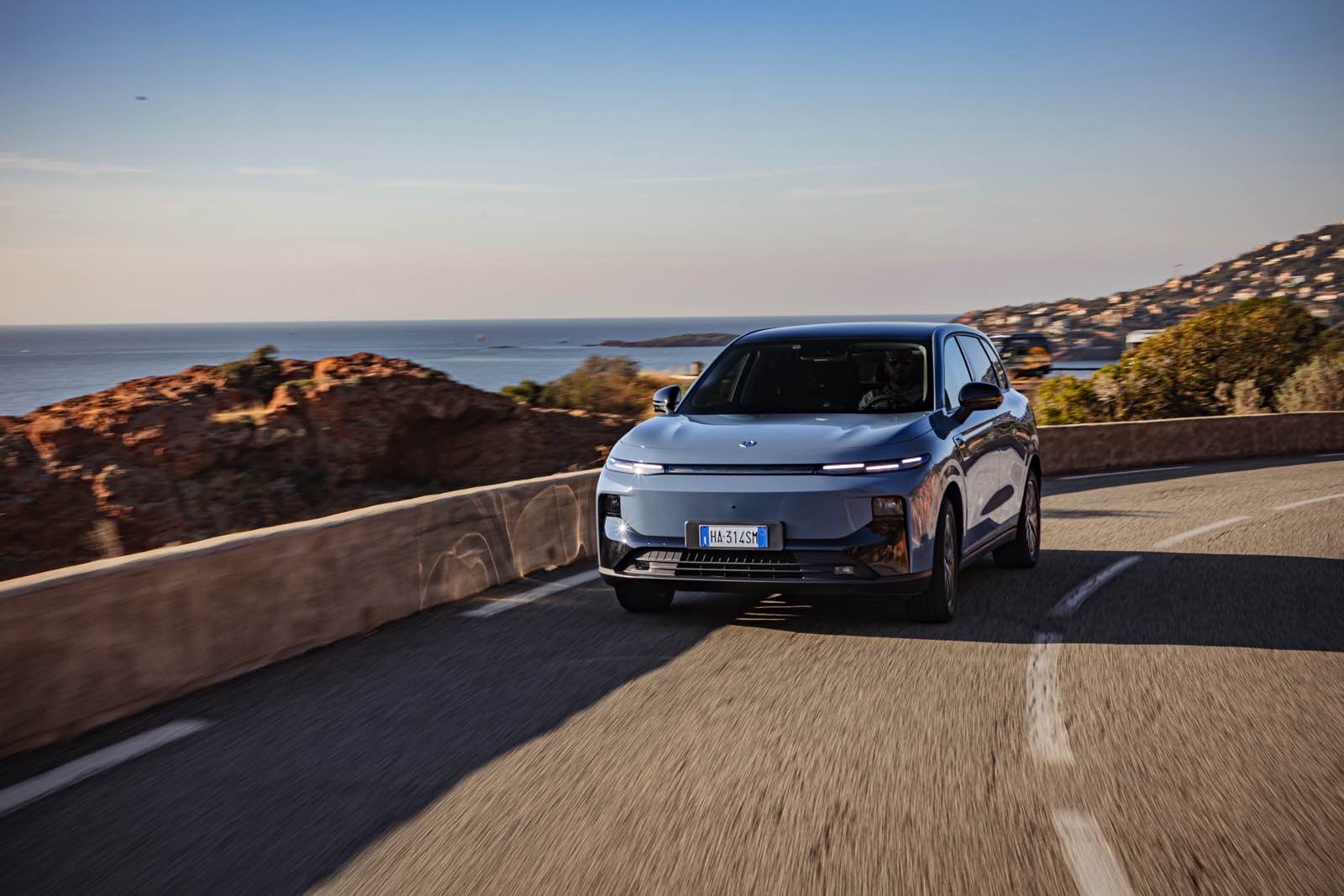 Auto ibrida che percorre una strada panoramica vista mare, con paesaggi di roccia e cielo sereno, perfetta per articoli su auto eco-friendly e viaggi di lusso.
