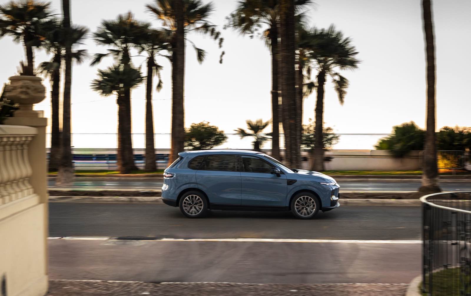 Auto SUV blu Leapmotor B10 in movimento lungo strada con palme, paesaggio soleggiato.