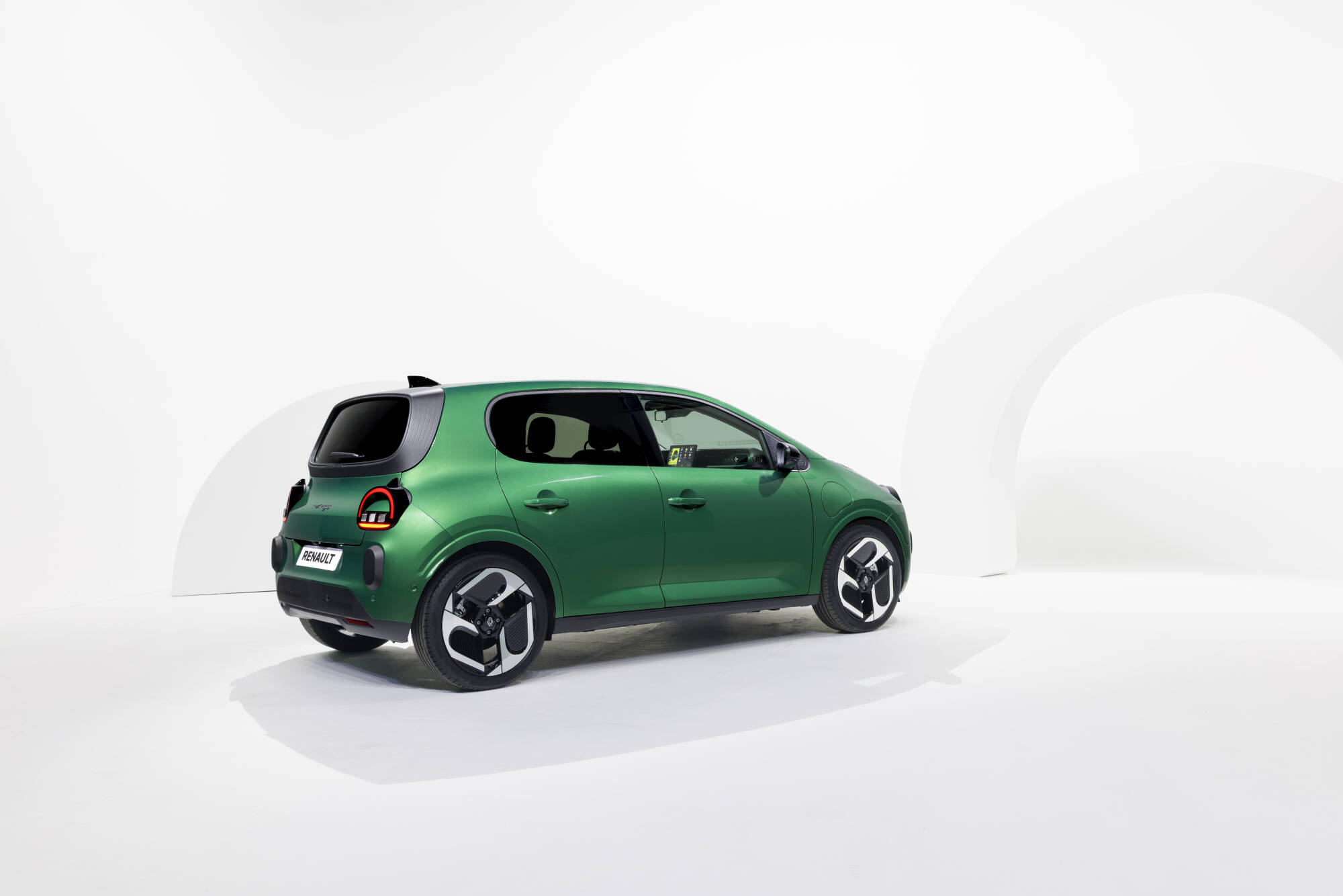 Auto Renault Twingo ed EV compatta di colore verde, modello Renault, in esposizione in uno studio minimalista bianco.