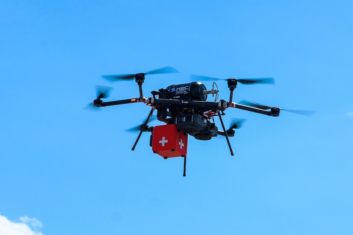 Dronte di emergenza medica con sistema di soccorso, dotato di casse di primo soccorso con croce svizzera, vola nel cielo blu per interventi rapidi in situazioni di emergenza.