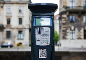 Parcometro con schermo digitale e QR code per pagamento tramite smartphone, sito per parcheggi a pagamento in città.