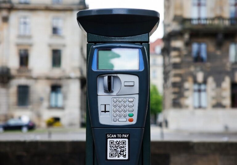 Parcometro con schermo digitale e QR code per pagamento tramite smartphone, sito per parcheggi a pagamento in città.