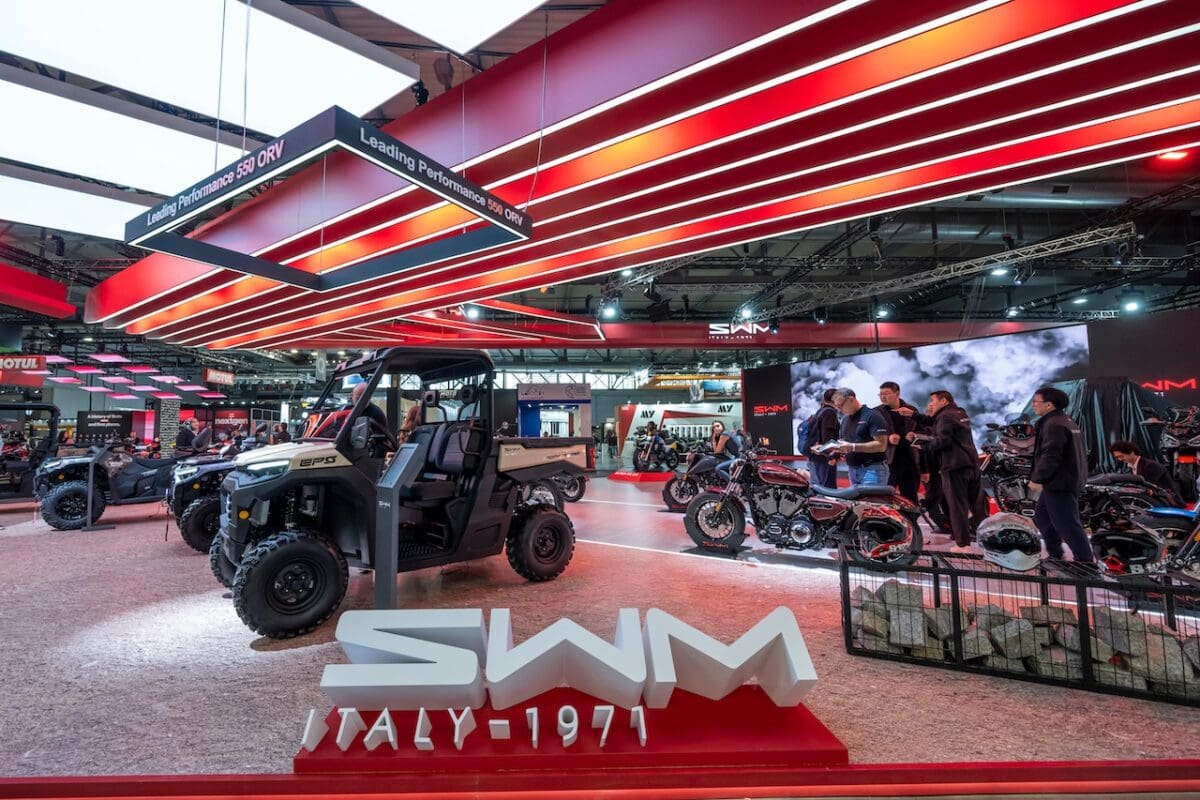 Design innovativo di veicoli off-road presso il salone motoristico internazionale, con moto, scooter e quad presentati in un ambiente moderno e tecnologico.