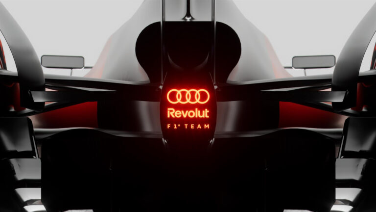 Dettaglio di un'auto da corsa Formula 1 Audi Revolution con logo illuminato rosso, stile futuristico, tecnologia avanzata, progettata per alte performance in circuito.