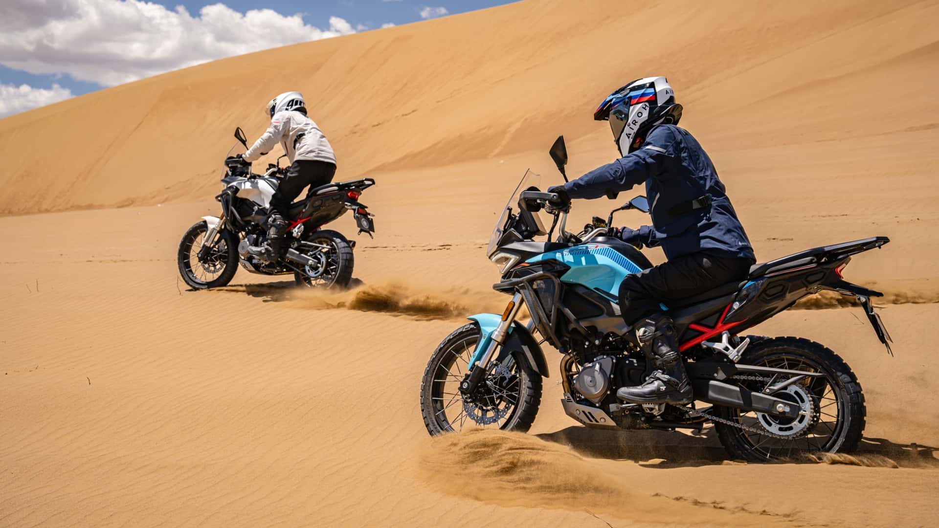 Motociclisti su moto Morbidelli T352X in ambientazione desertica con dune e cielo nuvoloso.
